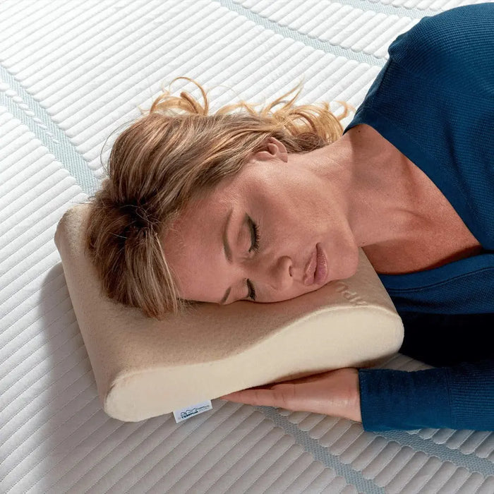 A woman in a blue outfit sleeping on the TEMPUR-Neck Travel Pillow.