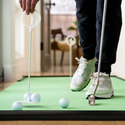 A person plays indoor mini golf on a BirdieBall Putting Green, using a putter to aim at golf balls toward a circular target, with BirdieBall Bumpers (Set of 2—Choose Size) acting as a stop for the balls.