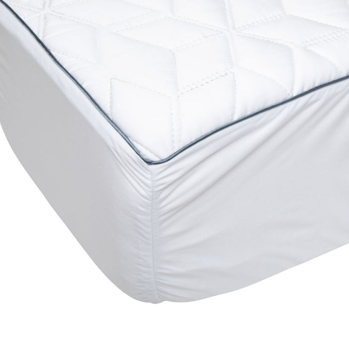 A close-up of a white mattress fitted sheet with a diamond-quilted top surface and a thin dark blue piping accent along the edge.