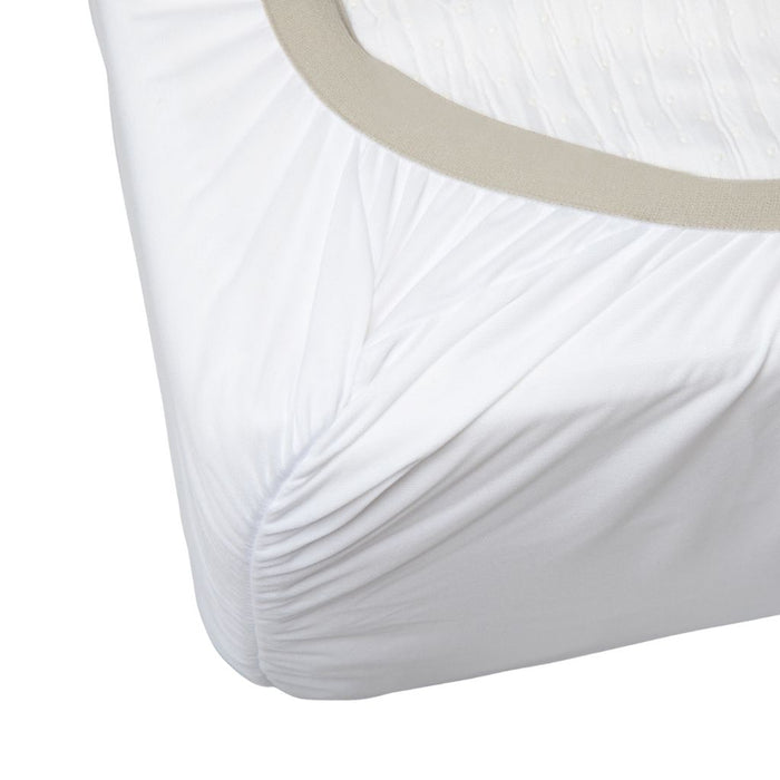 A close-up of a white fitted sheet or mattress cover with gathered pleats at the corner and a light beige elastic band around the mattress edge, shown on a white background.