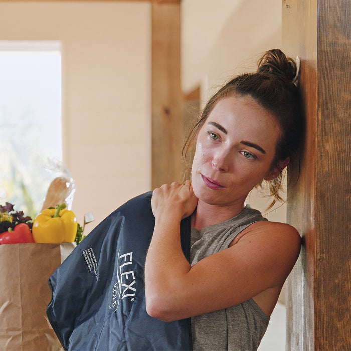 Woman leaning against a wall with a Flexi Kold cold pack in a kitchen.
