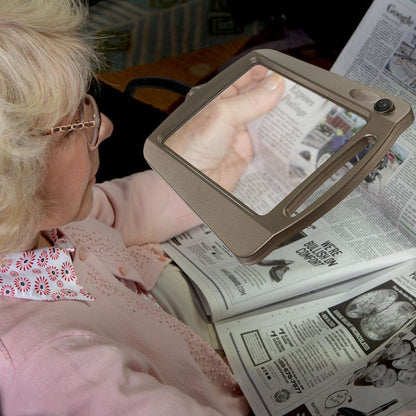 Person using a handheld magnifying glass to read a newspaper
