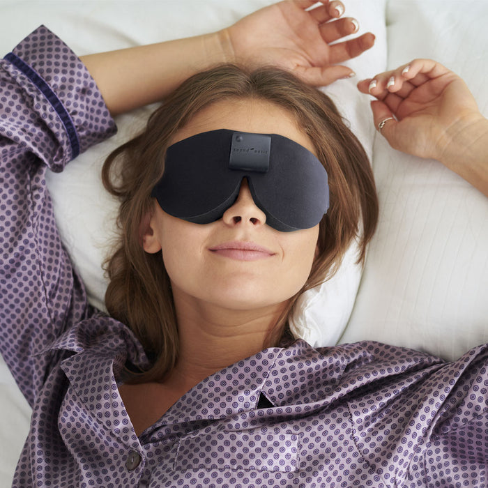 Woman wearing a sleep mask and purple pajamas lying on a white pillow.