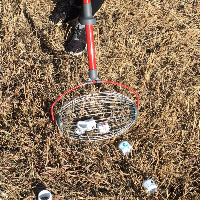 A person uses the BirdieBall Golf Ball Picker Upper - Shag Wheel to quickly collect plastic golf balls from dry grass during backyard practice.