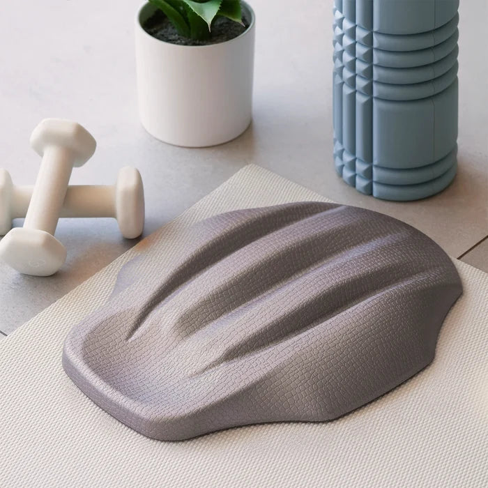 Gray lumbar nap decompression device on a light surface with a plant and dumbbells in the background
