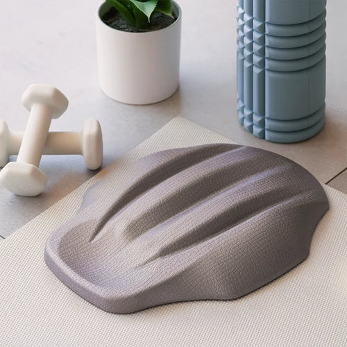 Gray lumbar nap decompression device on a light surface with a plant and dumbbells in the background