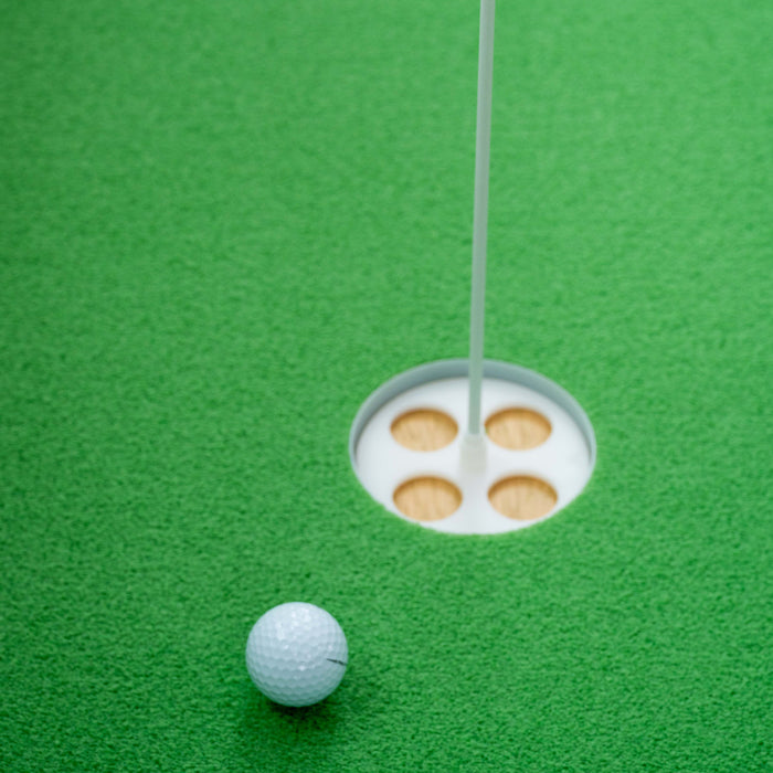 A white golf ball sits near a golf hole on the green, with the flagstick in the BirdieBall Putting Green Cup (Standard 1/2" deep), an essential accessory for any putting green.