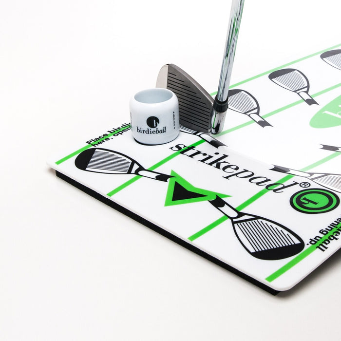 A BirdieBall StrikePad portable golf mat with strike zones, club illustrations, and a built-in swing path trainer is shown alongside a golf putter and a white BirdieBall cup on a white background.
