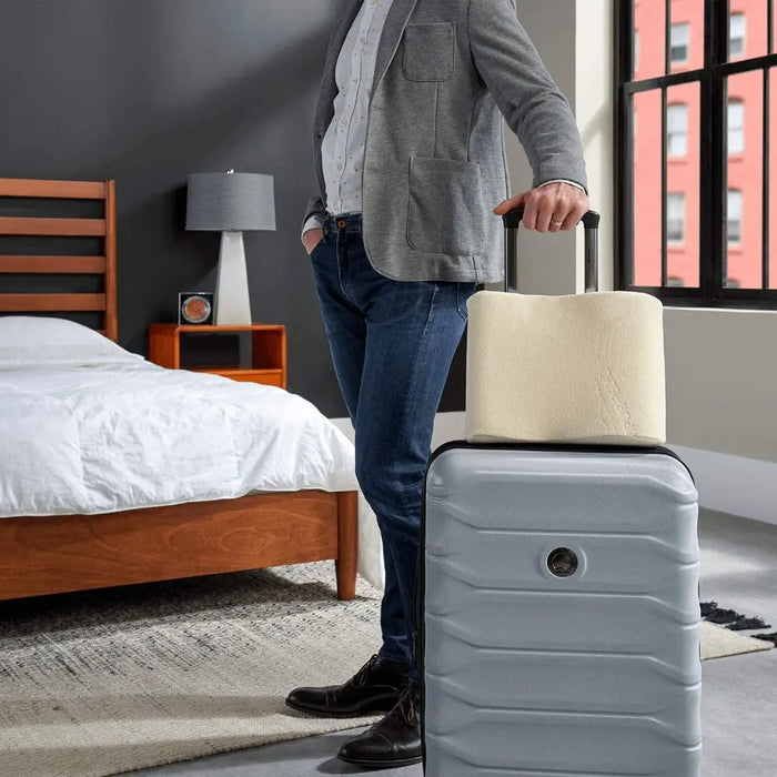 A man standing in a bedroom holding his suit case and the Tempur-Pedic Travel Neck Pillow.
