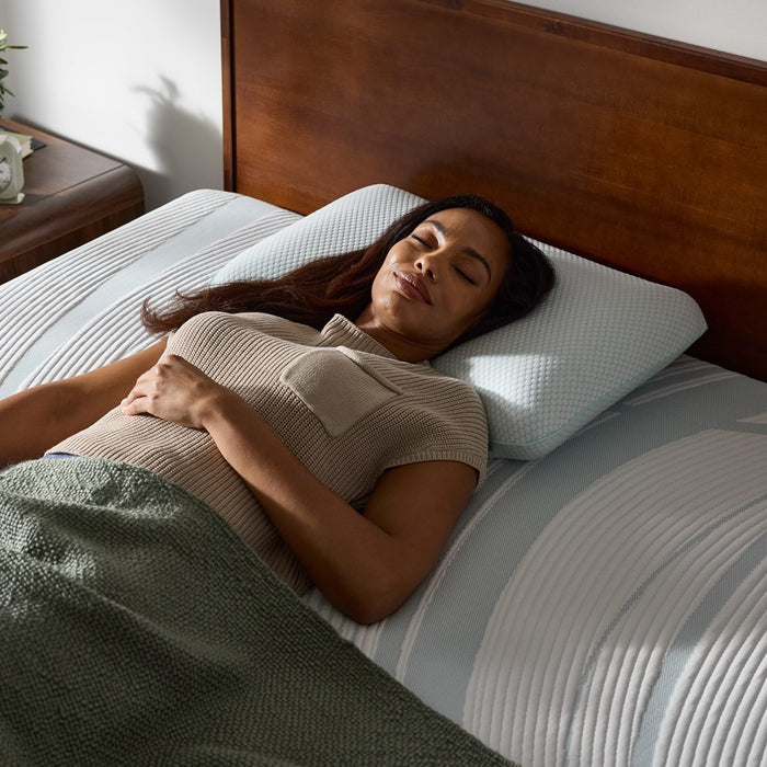 Woman sleeping on a bed with a white pillow and green blanket in a bedroom setting.