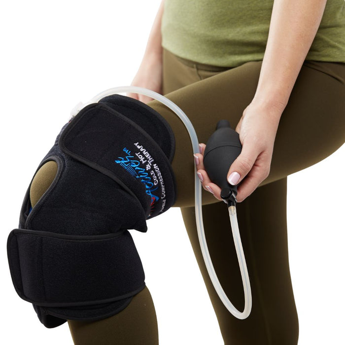 A person wearing a black knee support brace with an attached clear tube and holding a black pump bulb, shown against a white background.