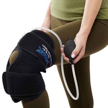 A person wearing a black knee support brace with an attached clear tube and holding a black pump bulb, shown against a white background.