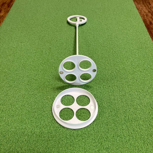 A BirdieBall Putting Green Cups and Flags set in white plastic, featuring circular holes, rests on a textured green surface with one cup separated and facing upward.