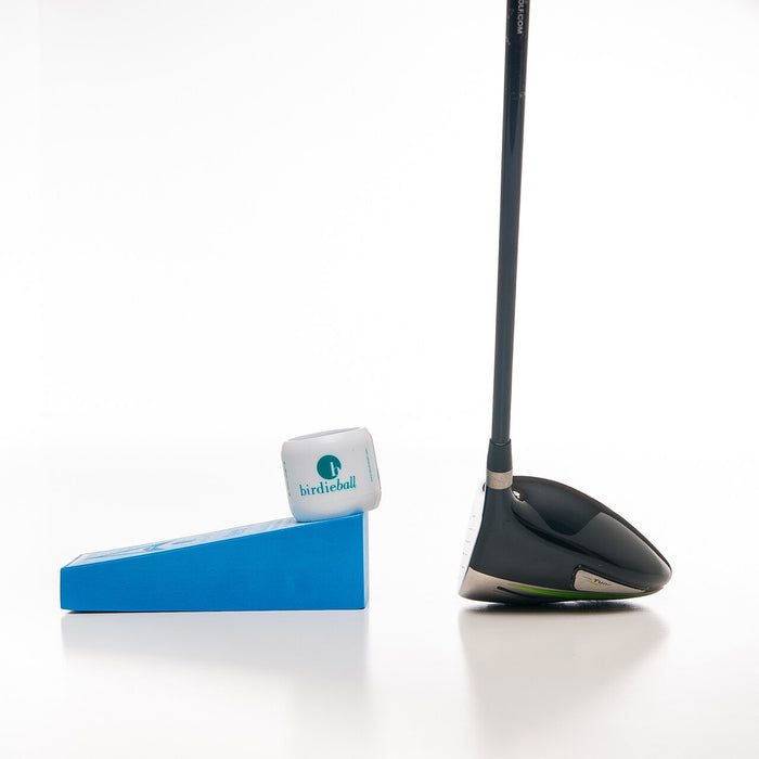 A BirdieBall Velocity Tee (for use with driver/woods) holds a golf ball on its blue wedge-shaped base, positioned next to a practice golf driver against a white background.